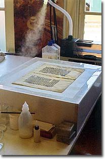 "Fibring" a parchment leave on a purpose-made vacuum table. The bullet holes are filled with parchment pulp.